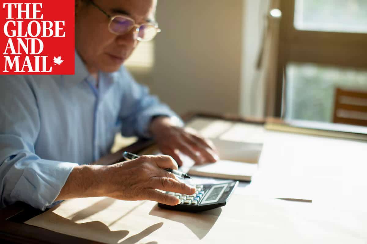 Middle aged man sitting at a desk using a calculator with Globe and Mail logo placed on top left corner